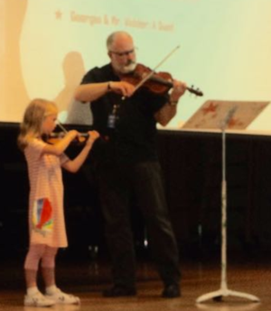 student and teacher playing violins